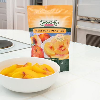 package of frozen peaches with a bowl of peaches in front of it in a kitchen setting