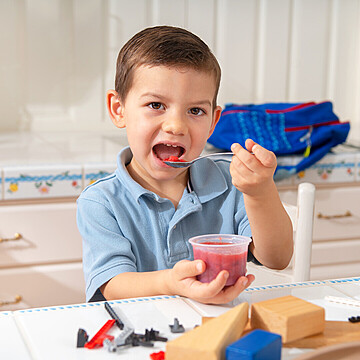 Young boy enjoying fruity dessert in a cheerful kitchen, surrounded by colorful building blocks.