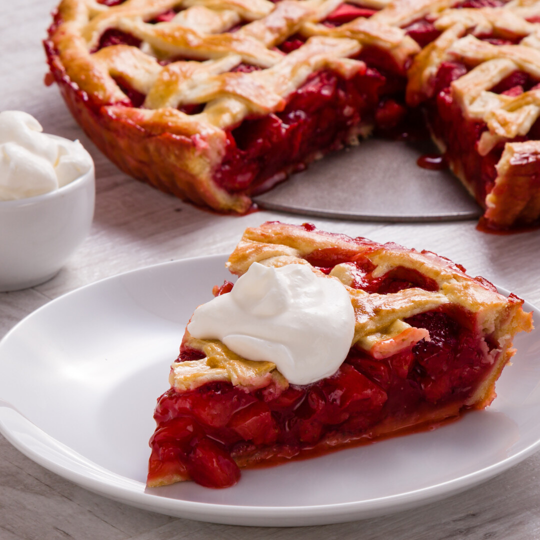 Delicious cherry pie slice with whipped cream on a rustic wooden table.