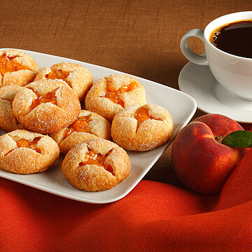 Delicious cookies with fruit jam, fresh peach, and coffee for a cozy treat.