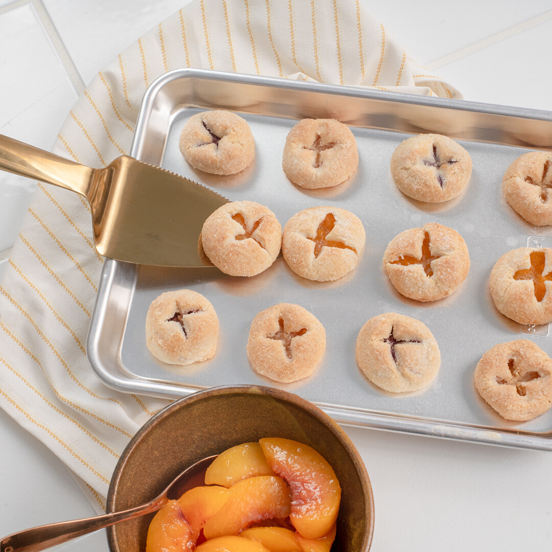 Freshly baked cookies and syrupy peach slices on an elegant tray for sharing.