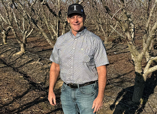 Man confidently stands in a barren orchard, showcasing agricultural life and seasonal change.