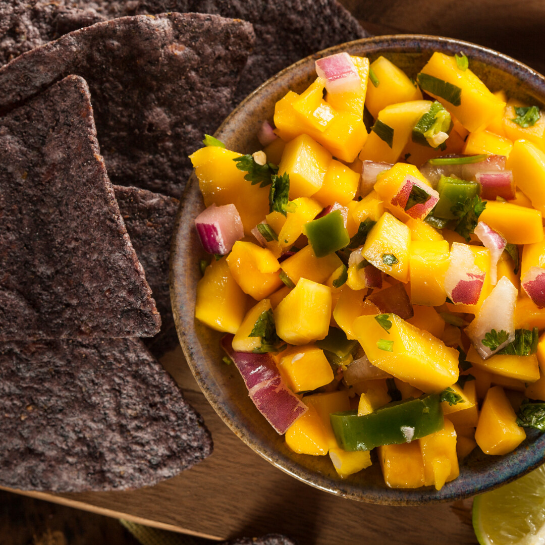 Fresh mango salsa served in a blue bowl with blue corn tortilla chips and lime.