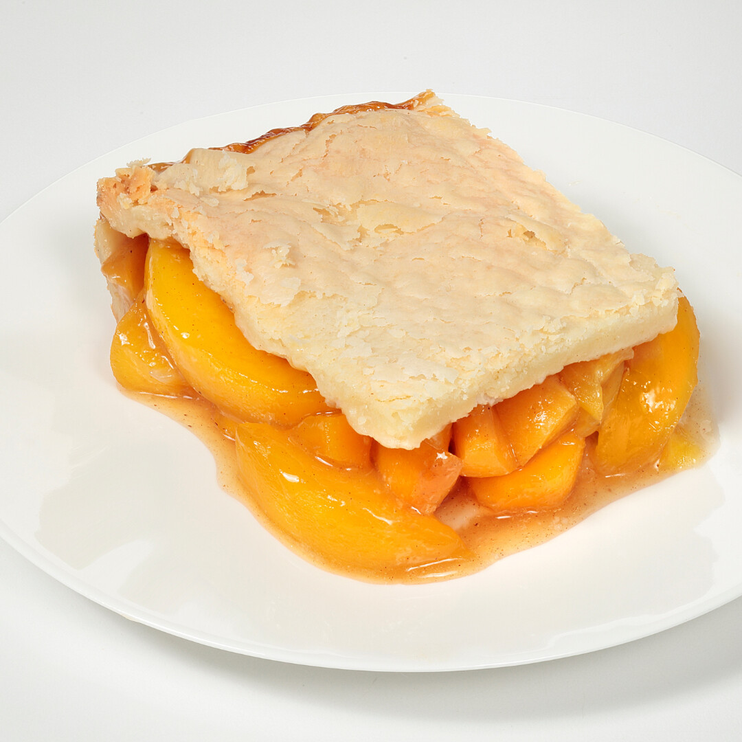 Delicious peach cobbler slice with flaky crust and juicy peach filling on a white plate.